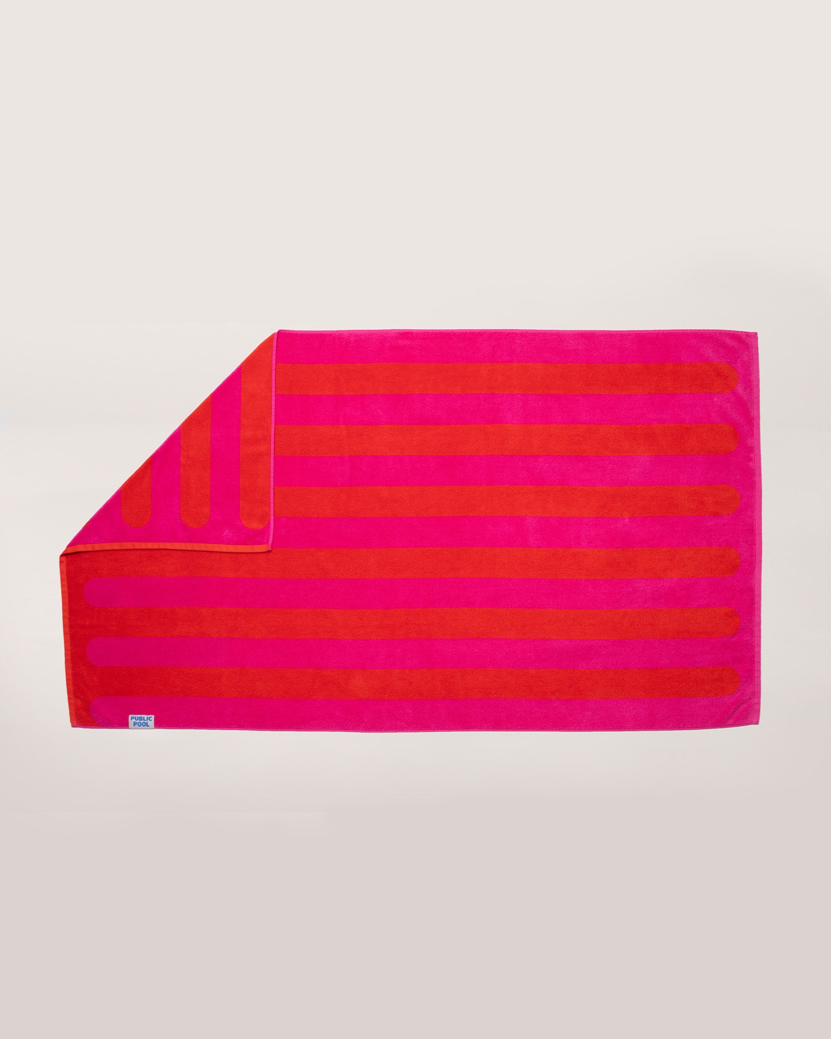 A red and magenta striped pool towel laying on a cream background. 