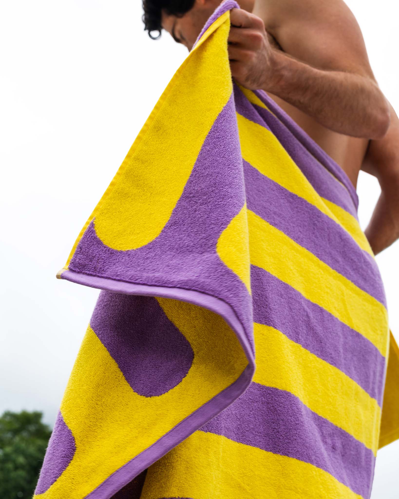 A man drying off with a yellow and purple striped towel. 