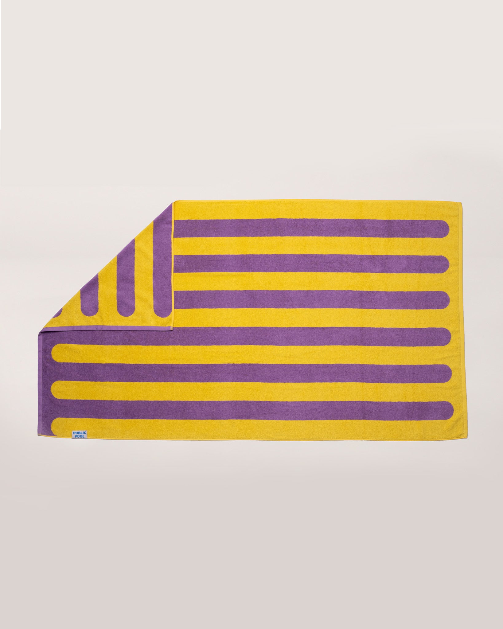 A yellow and purple striped pool towel laying on a cream background. 