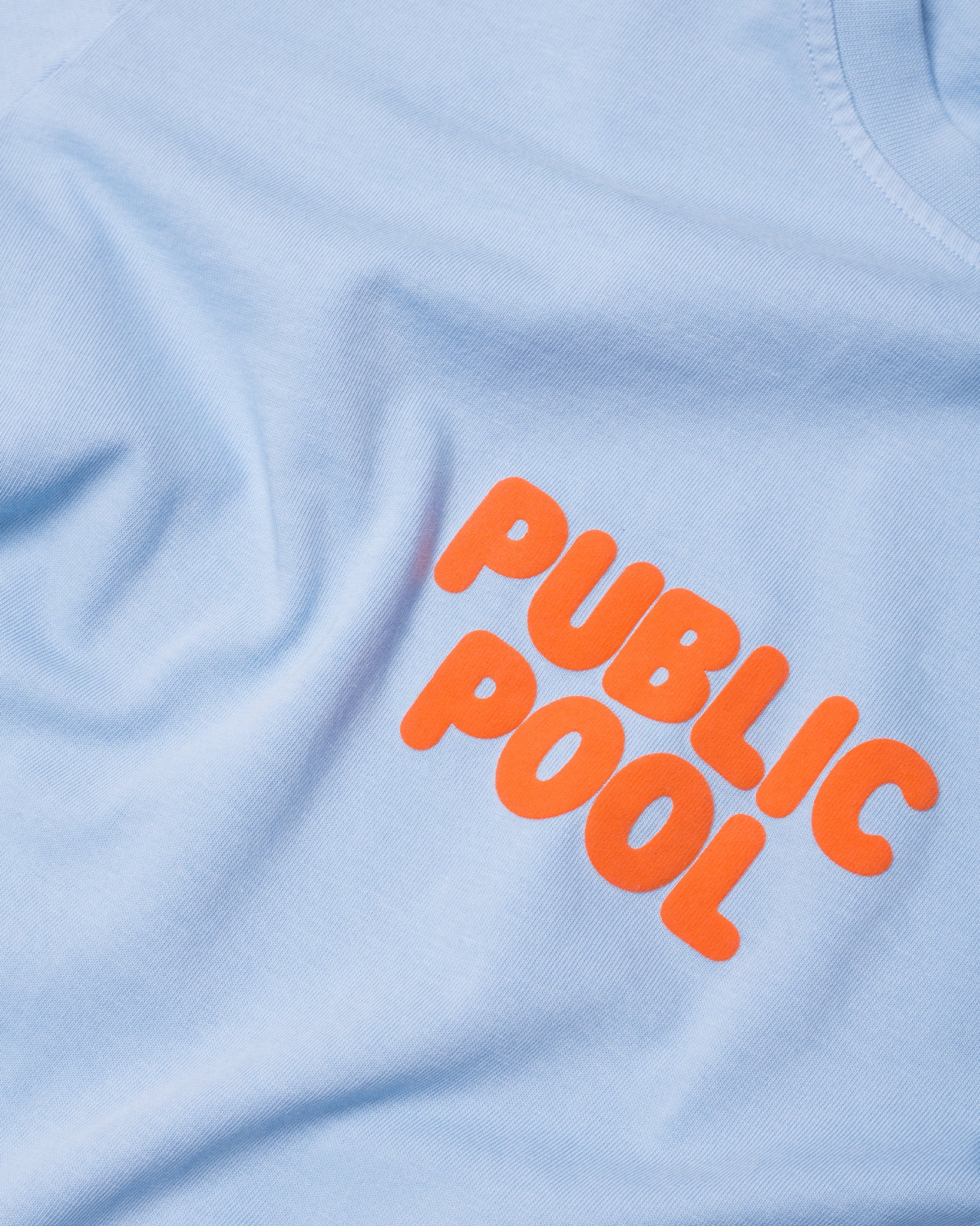 An image of the orange Public Pool logo on an baby blue shirt. 