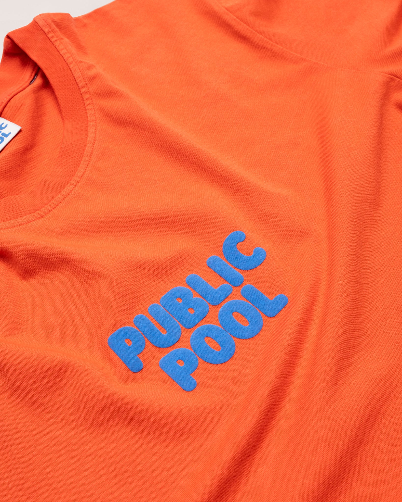A zoomed in image of the blue Public Pool logo on an orange shirt. 