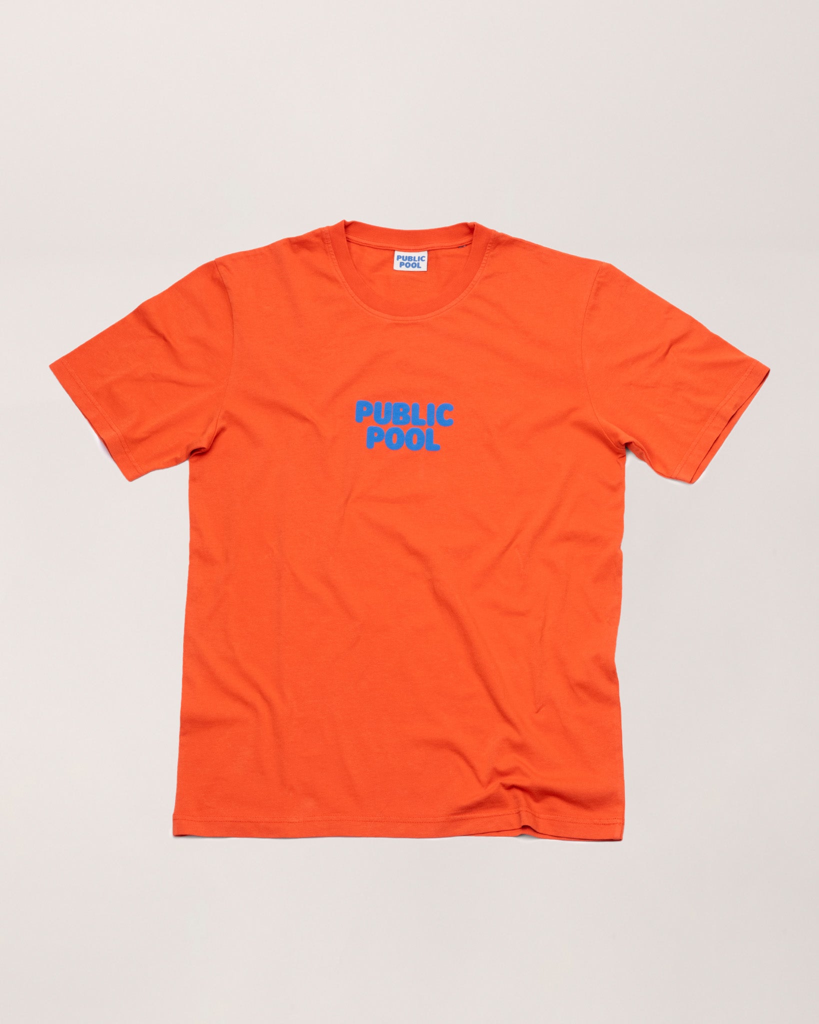An orange tee shirt with a blue Public Pool logo. 