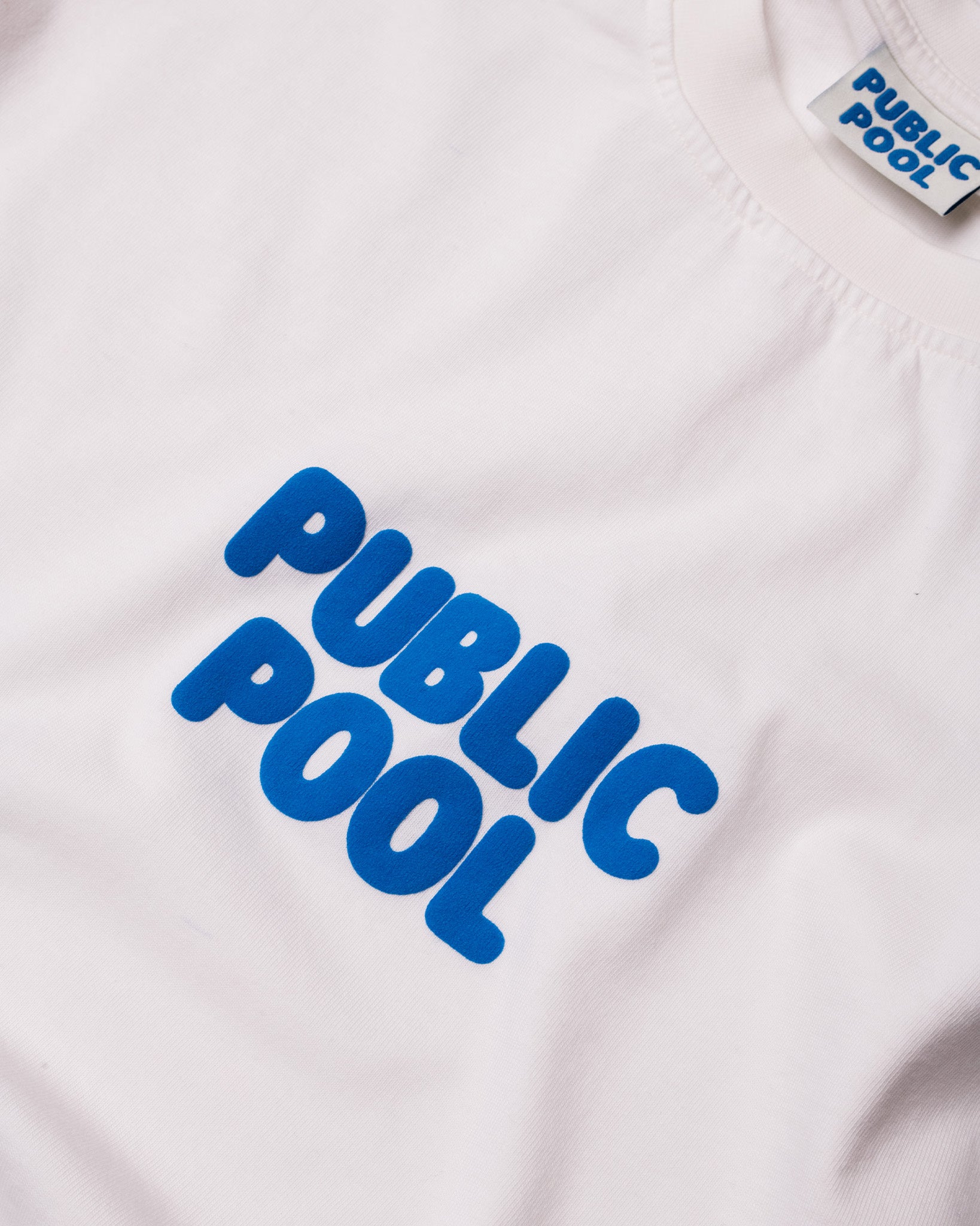 An image of the blue Public Pool logo on a white shirt. 