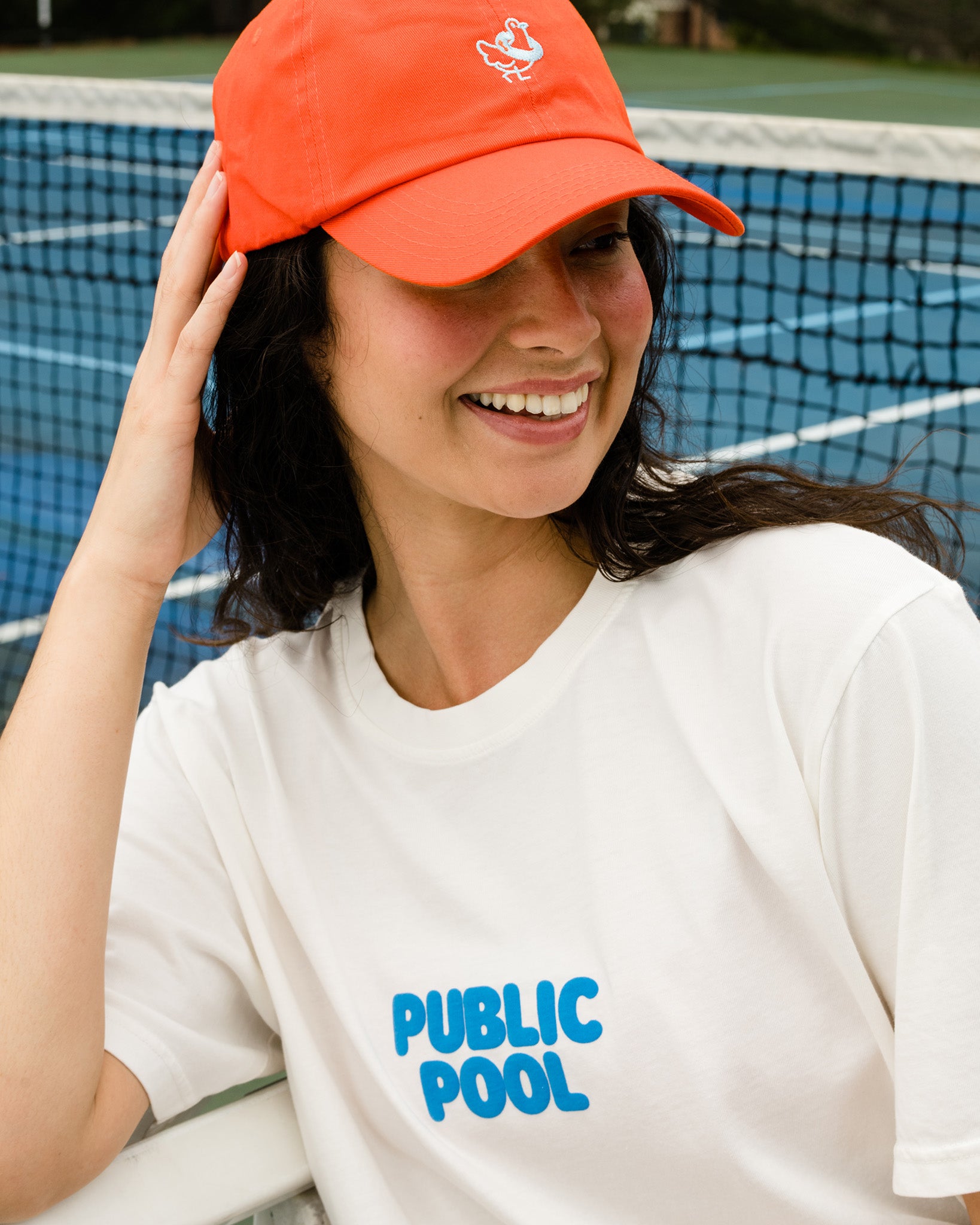 A woman wearing a white tee shirt with a blue Public Pool logo. 