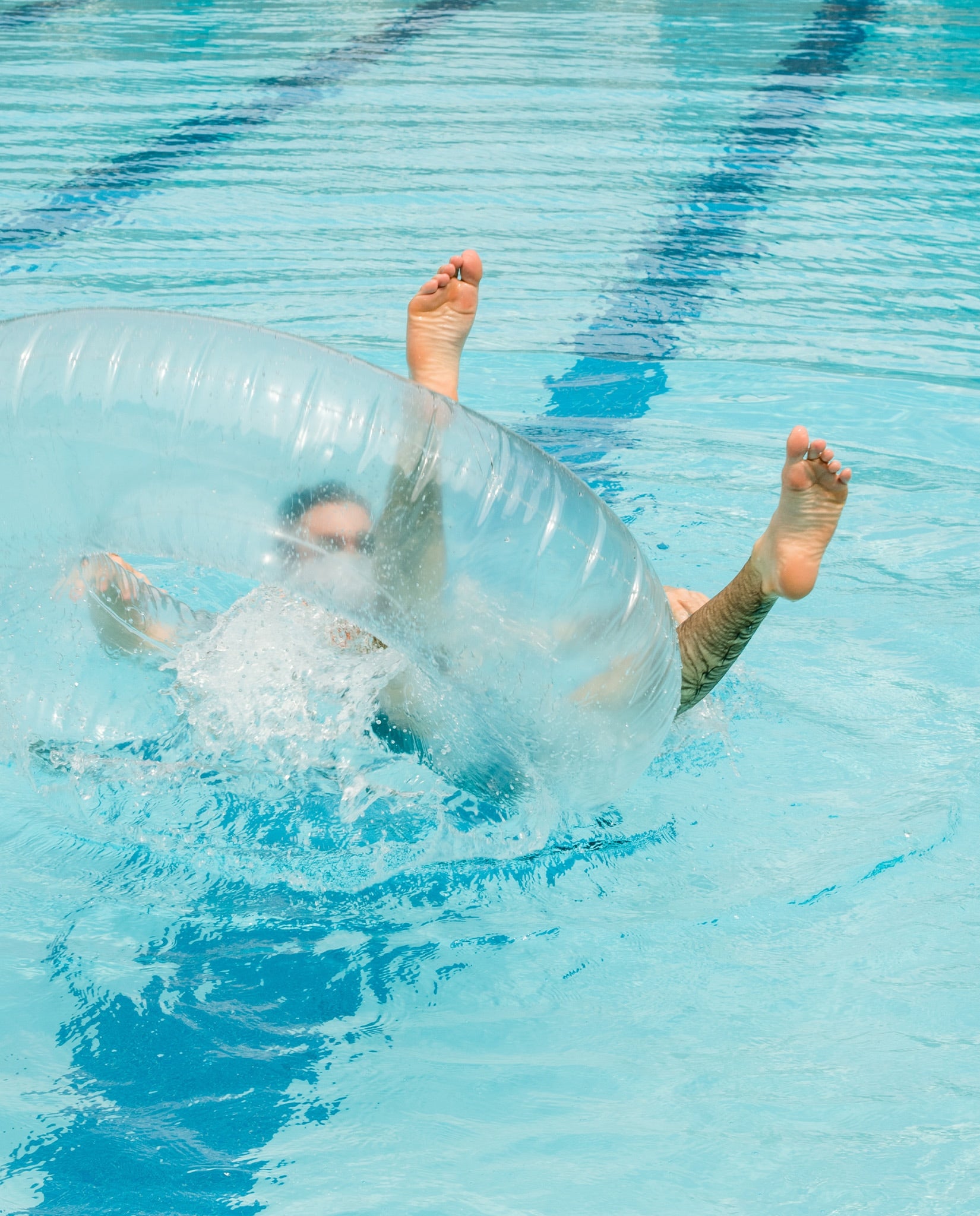A guy laughing and falling off of a pool float into the water. 