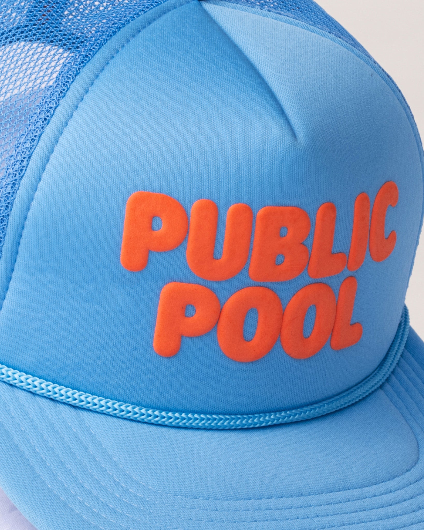 A detailed image of an orange Public Pool logo on a baby blue trucker hat. 