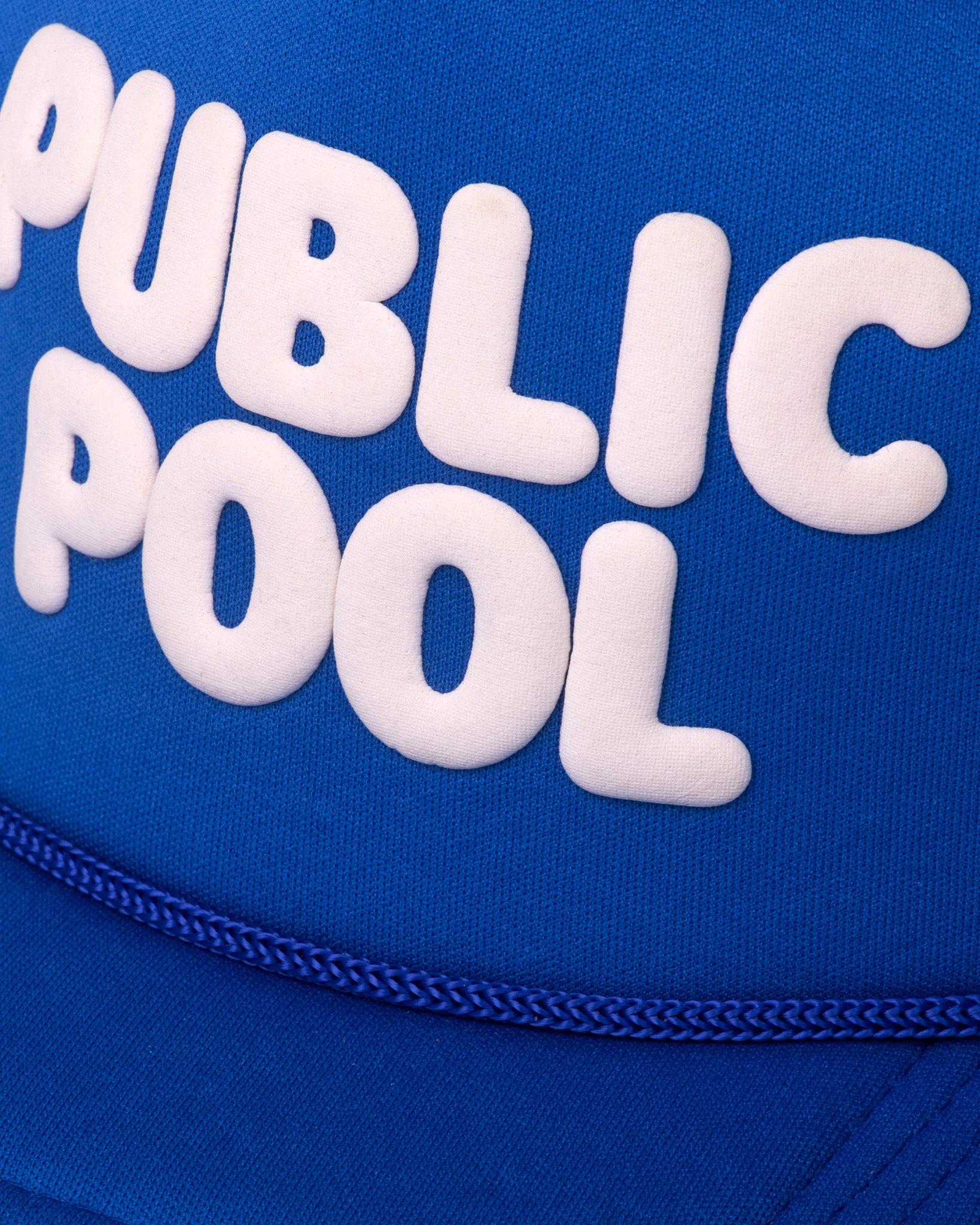 An image showcasing a puff print Public Pool logo on a blue trucker hat. 